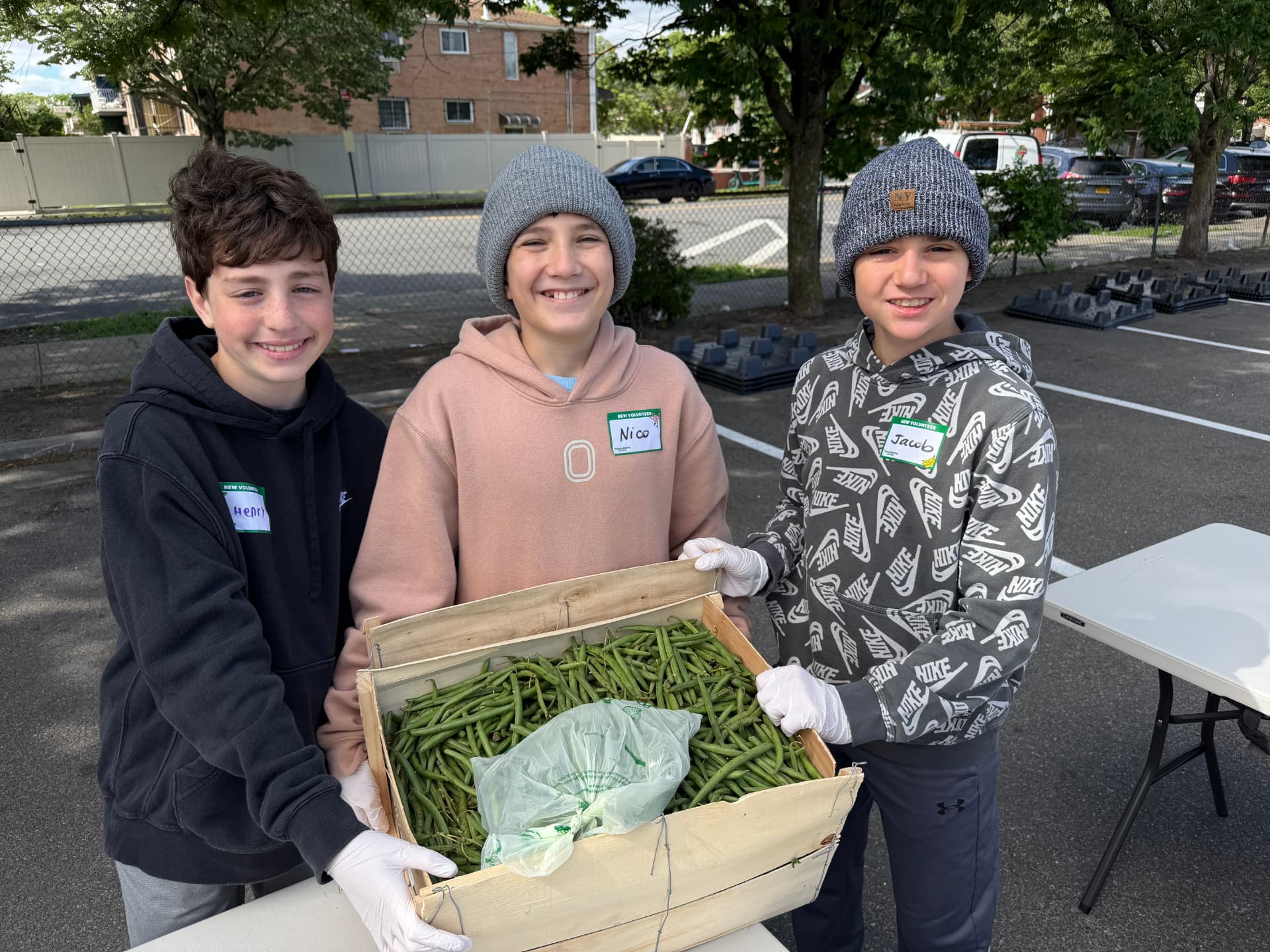 Henry and two friends in volunteer name tags holding a crate of green beans