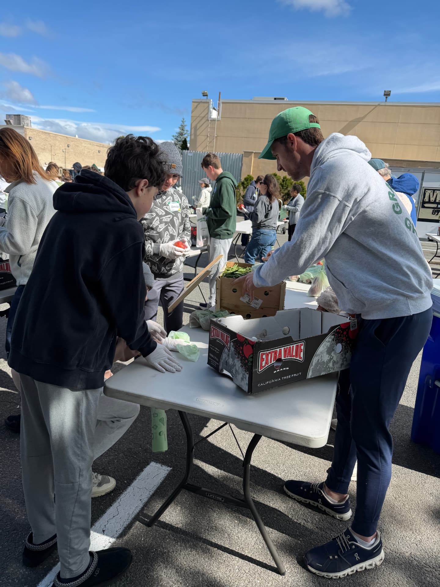 Volunteers packing produce into boxes at folding tables in a parking lot